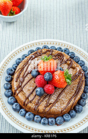 Big chocolate Cheesecake mit Erdbeeren Heidelbeeren Himbeeren auf einer runden Platte. Stockfoto