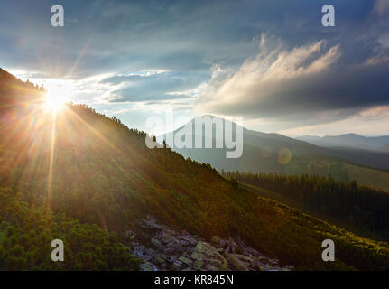 Letzte Sonnenstrahlen am Abend Himmel mit Wolken über Syniak Berg. Sommer Sonnenuntergang Blick von Homiak Berg, Gorgany, Karpaten, Ukraine. Einige sun flare Stockfoto