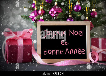 Schiefertafel mit französischen Text Joyeux Noel Et Bonne Annee bedeutet, frohe Weihnachten und ein glückliches Neues Jahr. Weihnachtsbaum mit Rosenquarz Kugeln, Schneeflocken und Bokeh Wirkung. Geschenke Vor Zement Hintergrund. Stockfoto