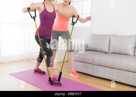 Leistungsstarke attraktiven weiblichen Fitness Mädchen mit Resistance Band Workout training Körper mit Ihrem Lehrer zu Hause. Stockfoto