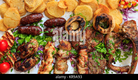 Zyprischen Köstlichkeiten. Gemischtes Fleisch vom Grill mit Gemüse und Kartoffeln auf weiße Oberfläche. Nähe zu sehen. Stockfoto