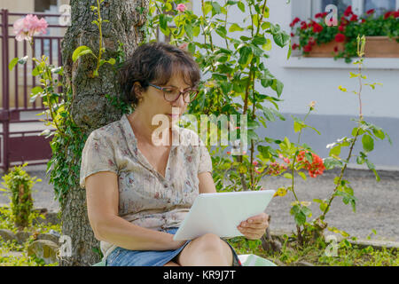 Reife Frau sitzend mit einem Tablett in den Garten Stockfoto