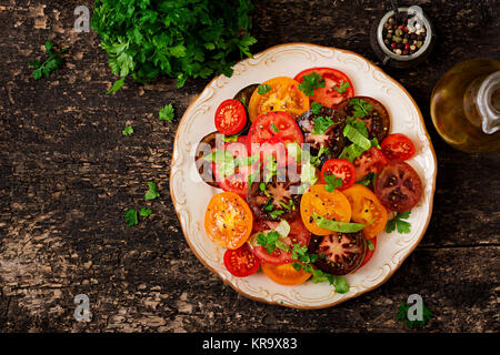 Sommer Salat von Tomaten in verschiedenen Farben mit grünen Kräutern und Pfeffer. Ansicht von oben Stockfoto