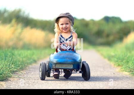 â lachendes kleines Mädchen mit nostalgischem Tretauto Stockfoto