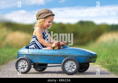 â lachendes kleines Mädchen mit nostalgischem Tretauto Stockfoto