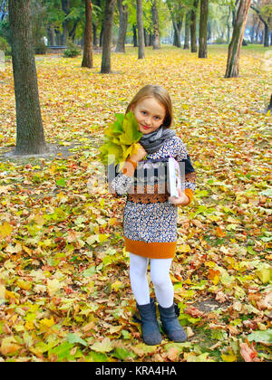 Kleines Mädchen mit gelben Blättern und buchen Sie im Park Stockfoto