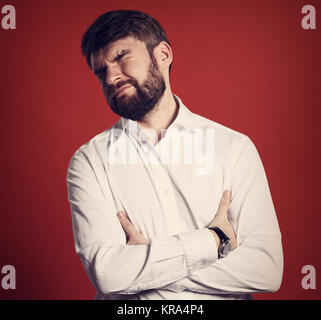 Angewidert bärtigen Geschäftsmann mit geschlossenen Augen und unglückliches Gesicht in Fashion white style Hemd. Closeup Portrait auf rotem Hintergrund Stockfoto