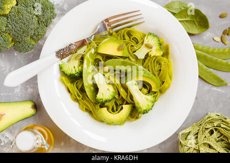 Gesunder Spinat Nudeln mit Brokkoli, Avocado, Kürbiskerne und grünen Erbsen. Ansicht von oben. Vegane Ernährung Essen Konzept. Stockfoto