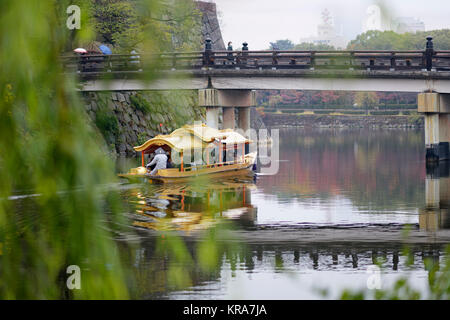 Die Leute, die eine Fahrt auf Osaka-jo Gozabune Boot in Osaka Castle Park inneren Burggraben Kanal vorbei unter Brücke Gokurakubashi auf einem nebligen Herbstmorgen. Chu Stockfoto