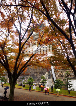 Menschen mit Sonnenschirmen am Schloss Osaka historische Sicht, Osakajo, hinter bunten roten Baum versteckt Blätter auf einem ruhigen Misty regnerischen Herbstmorgen. Osaka, Stockfoto