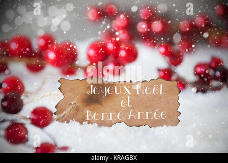 Verbrannt Label mit französischen Text Joyeux Noel Et Bonne Annee bedeutet, frohe Weihnachten und ein glückliches Neues Jahr. Rot Weihnachten Dekoration auf Schnee. Zement Wand als Hintergrund mit Bokeh Effekt und Schneeflocken Stockfoto