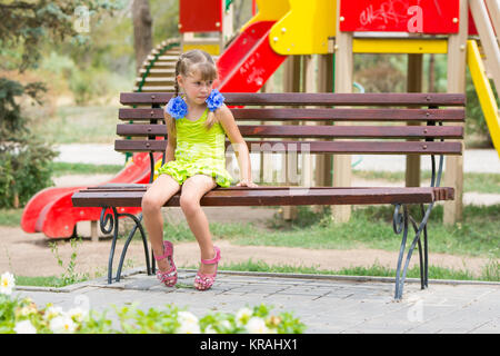 Aufgeregt Mädchen Biss ihre Lippen während Sie sitzen auf der Bank vor dem Hintergrund des Spielplatzes Stockfoto