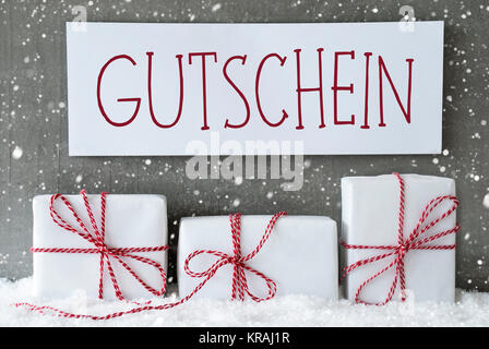 Etikett mit deutschem Text Gutschein Gutschein bedeutet. Drei Weihnachten Geschenke oder Präsentiert auf Schnee. Zement Wand als Hintergrund mit Schneeflocken. Moderne und den urbanen Stil. Stockfoto