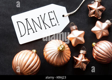 Etikett mit deutschem Text Danke, Danke. Bronze Christbaum Kugeln auf schwarzem Papier Hintergrund. Weihnachtsdekoration oder Textur. Flach anzeigen Stockfoto