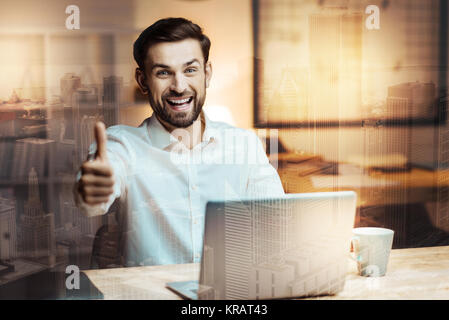 Optimistischer Mann mit Daumen hoch während der Arbeit am Laptop Stockfoto