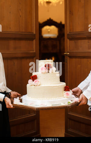 Multi Level weiße Hochzeitstorte auf einem Sockel und Blumen an der Spitze. Stockfoto