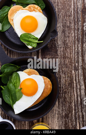 Valentinstag Frühstück oder Brunch. Hausgemachte Herzform Spiegelei und Pfannkuchen in Gusseisen Skillet mit Spinat, Orangensaft und Kaffee. T Stockfoto