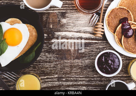 Valentinstag Frühstück oder Brunch. Hausgemachte Herzform Spiegelei und Pfannkuchen in Gusseisen Skillet mit Spinat, Kürbis Pfannkuchen mit Marmelade, orange Stockfoto