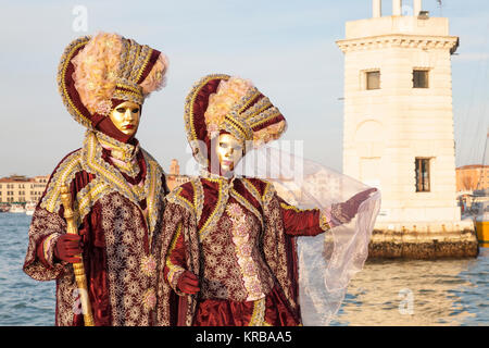 Karneval in Venedig, Venetien, Italien, Paar in reich bestickt rot Kostüme im Santa Maria Giorgio Leuchtturm bei Sonnenuntergang posing Stockfoto