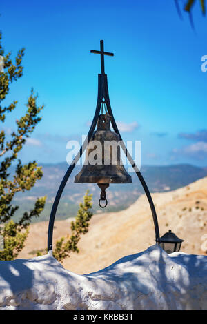 Bronzene Glocke mit Kreuz an der Wand von Tsambika Kloster (Rhodos, Griechenland) Stockfoto