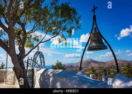 Bronzene Glocke mit Kreuz an der Wand von Tsambika Kloster (Rhodos, Griechenland) Stockfoto