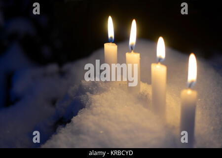 Vier weiße brennende Kerzen draußen im Schnee Stockfoto