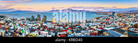 Antenne Panorama der Innenstadt von Reykjavik bei Sonnenuntergang mit bunten Häusern und schneebedeckten Bergen im Hintergrund Stockfoto