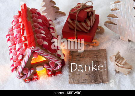 Etikett mit deutschem Text Danke, Danke. Lebkuchenhaus auf Schnee mit Weihnachten Dekoration wie Bäume und Elche. Schlitten mit Weihnachten Geschenke oder präsentiert. Stockfoto