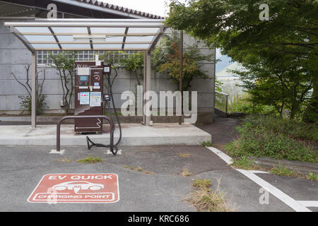 Japanische moderne elektrische Auto aufladen an Station Dock. EV QUICK Ladestation Zeichen die WADB/BOAD und Elektroauto Ladestation Punkt im Park Stockfoto