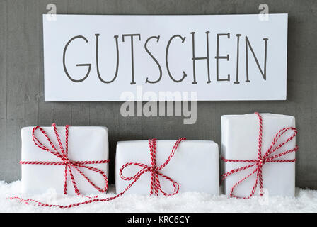 Etikett mit deutschem Text Gutschein Gutschein bedeutet. Drei Weihnachten Geschenke oder Präsentiert auf Schnee. Zement Wand als Hintergrund. Moderne und den urbanen Stil. Karte für den Geburtstag oder Seasons Greetings. Stockfoto