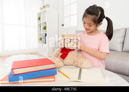 Hübsche attraktive Mädchen helfen ihr Bär Spielzeug Brille trägt, wenn Sie das Schreiben der Schule zu Hause. Stockfoto