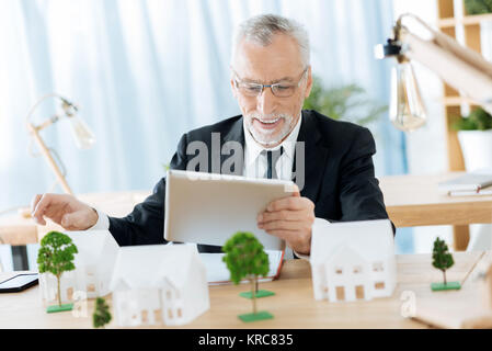 Positive Arbeiter am Tisch sitzen und und lächelnd eine Minianwendung Stockfoto