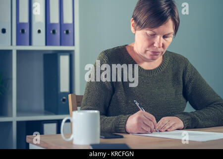 Geschäftsfrau Unterzeichnung Papiere oder das Schreiben von Notizen in Small Business Office Interior Stockfoto