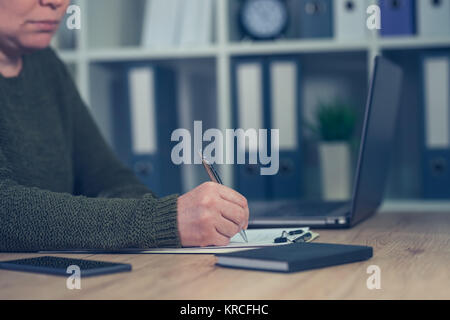 Geschäftsfrau Unterzeichnung Papiere oder das Schreiben von Notizen in Small Business Office Interior Stockfoto