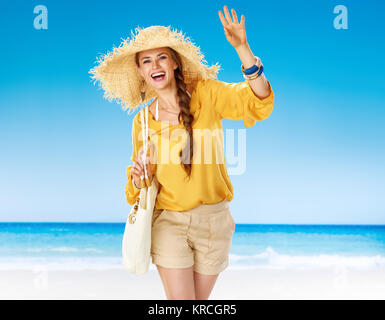 Perfekte Sommer. lächelnd passende Frau in kurzen Hosen und gelbe Bluse mit weißem Strand Beutel, der am Ufer des Meeres handwaving Stockfoto