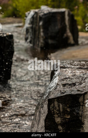 Wasserfontänen aus einem schwarzen Rock im Park Stockfoto