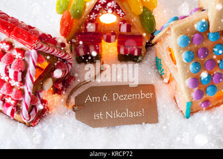 Etikett mit deutschem Text am 6. Dezember ist Nicholas bedeutet Dezember 6 ist Nikolaus Tag. bunte Lebkuchen Haus auf Schnee und Schneeflocken. Weihnachtskarte für Seasons Greetings Stockfoto