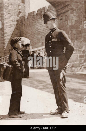 Eine junge Kolumne, Johnny Wilson, aus Pappel, East London, Chatten mit einem Polizisten in Caernarvon, wo er gegangen ist die Einsetzung der Prinz von Wales zu beobachten. Während dort, er ist beauftragt worden, die Stiefel der zahlreichen Mitglieder der Metropolitan Police, die caernarvon auf besondere Pflicht gegangen sind zu reinigen. Datum: Juli 1911 Stockfoto