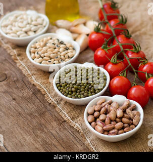 Hülsenfrüchte in Schalen, Tomaten, Knoblauch und Olivenöl auf hölzernen Tisch Stockfoto