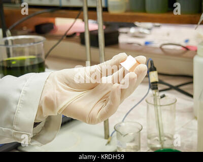 Hand in einem gummihandschuh hält eine Metall Muster in einem chemischen Labor Stockfoto