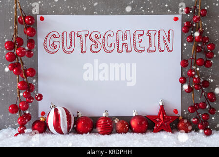 Etikett mit deutschem Text Gutschein Gutschein bedeutet. Rot Weihnachten Dekoration wie Bälle auf Schnee. Urban und modernen Zement Wand als Hintergrund mit Schneeflocken. Stockfoto