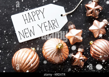 Etikett mit englischem Text Frohes neues Jahr. Bronze Christbaum Kugeln auf schwarzem Papier Hintergrund mit Schneeflocken. Weihnachtsdekoration oder Textur. Flach anzeigen Stockfoto