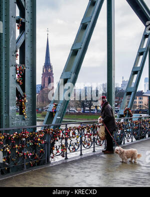 Frankfurt, Deutschland. Mann mit Hund auf Eiserner Steg, Bügeleisen Fußgängerbrücke, eiserne Brücke über den Fluss Main, Blick auf Kirche, Gebäude, liebe Schlösser. Th Stockfoto