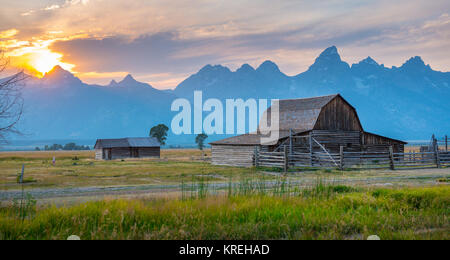 Die untergehende Sonne taucht über Teton Bergkette und historischen John moulton Scheune auf Mormon Reihe, Grand Tetons National Park, Teton County, Wyoming Stockfoto