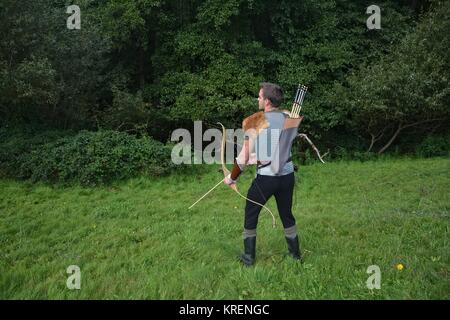 â Â Â Â junger mittelalterlicher Bogenschütze mit Kettenpost, Bogen und Pfeil in der Natur beim Verbeugen Stockfoto