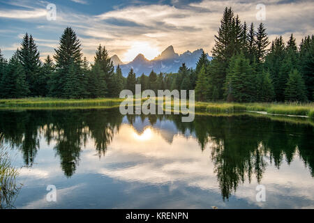 Sonnenlicht kriecht hinter Gipfeln der Teton Bergkette mit gläsernen Wassers im Vordergrund, Grand Tetons National Park, Teton County, Wyoming Stockfoto