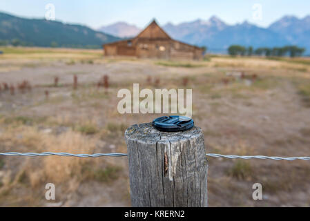 Objektivkappe auf hölzernen Zaun Pfosten vor T.A. Molton Scheune, Grand Tetons National Park, Teton County, Wyoming platziert Stockfoto