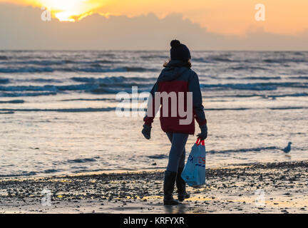 Frau zu Fuß an der Strandpromenade am Strand mit einem Tesco Shopping Bag, im Winter in Großbritannien. Stockfoto