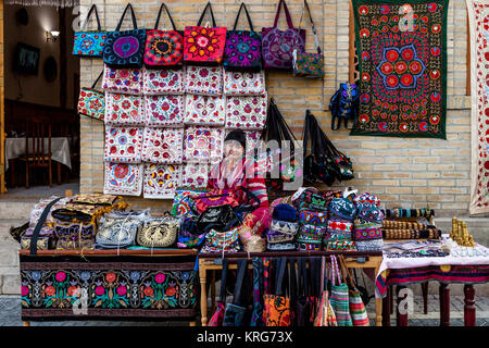 Eine usbekische Frau in traditioneller Tracht mit Souvenirs aus Ihrem Stall, Buchara, Usbekistan Stockfoto