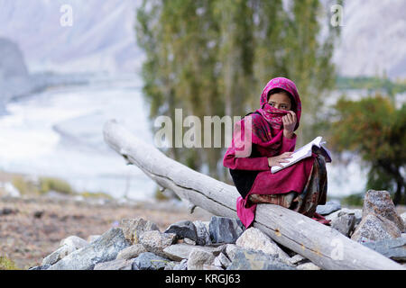 Eine junge balti Mädchen sitzt auf einem Ast und über ihr Gesicht mit einem bunten Schal, Turtuk, Nubra Valley, Ladakh, Jammu und Kaschmir, Indien. Stockfoto